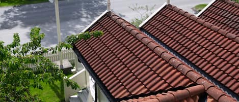 Un edificio residencial con techo de tejas rojas, cerca blanca y vista a la calle.