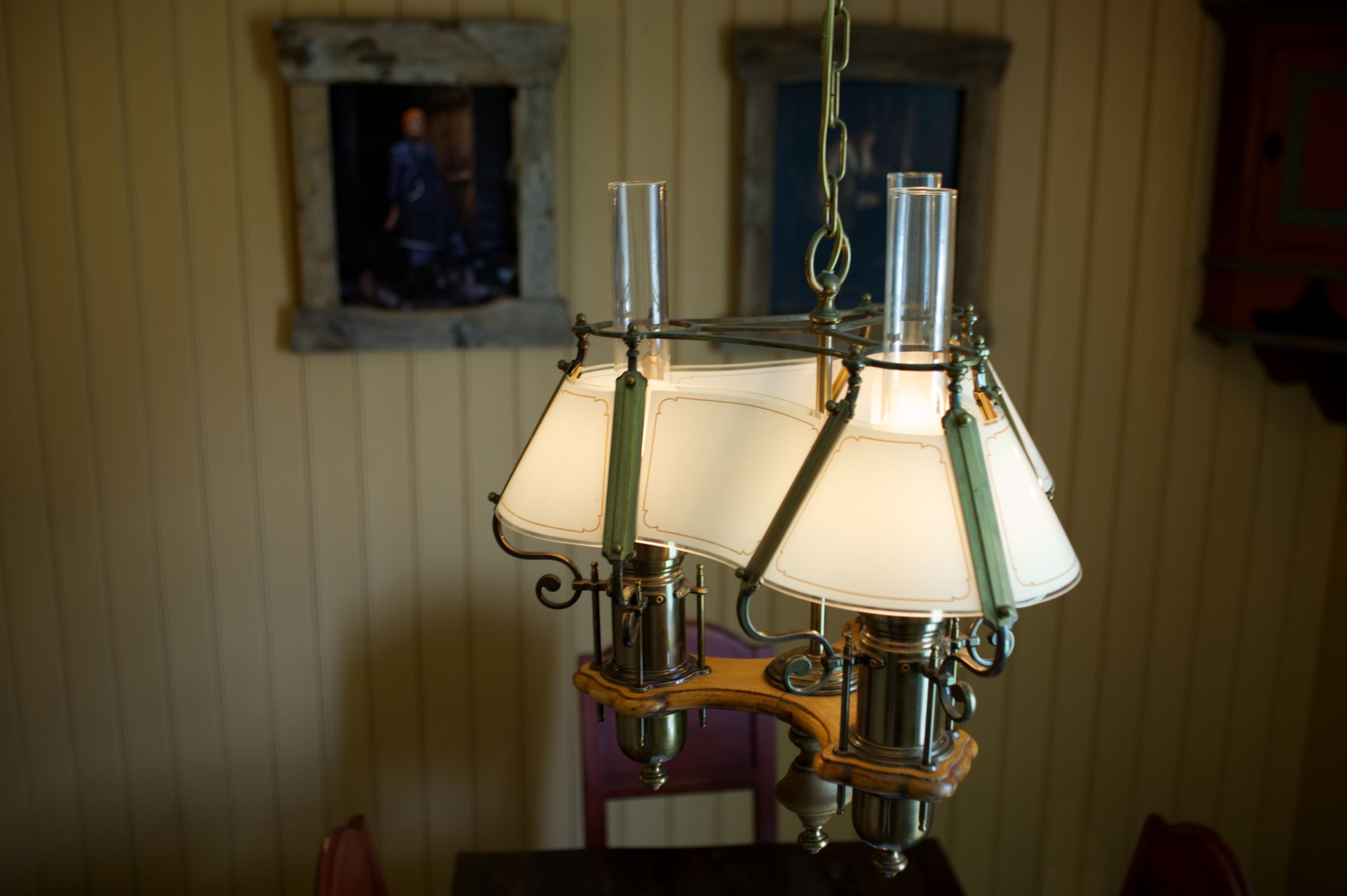 A chandelier with multiple lampshades in a room with vertical paneling and a framed picture on the wall.