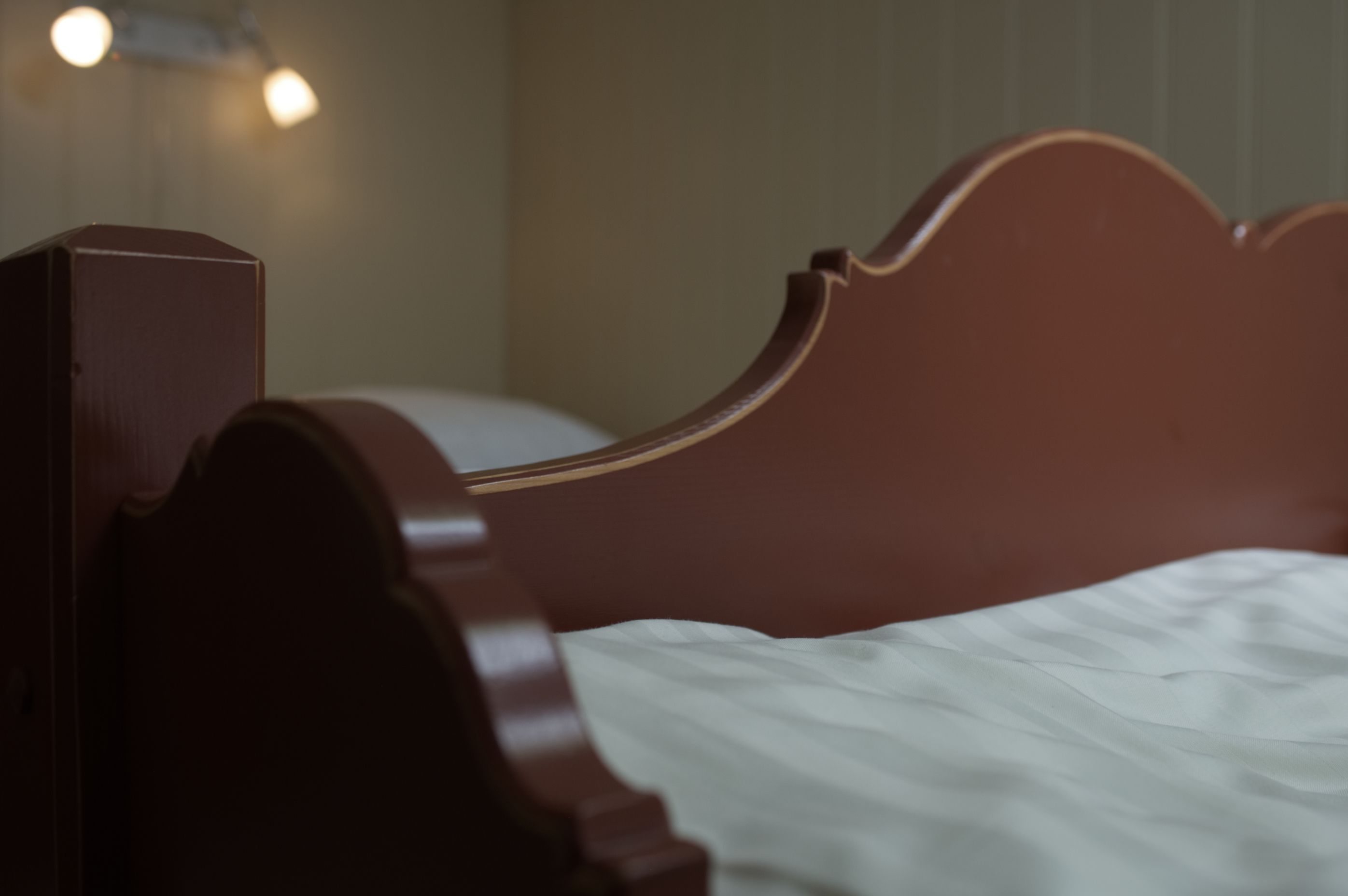 A wooden headboard with a curved design, a white bedspread, and a wall-mounted light fixture.