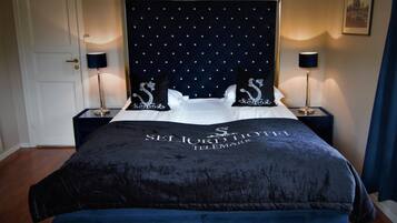 A hotel room with a large bed, a dark headboard with a pattern, two bedside tables with lamps, and a framed picture on the wall.