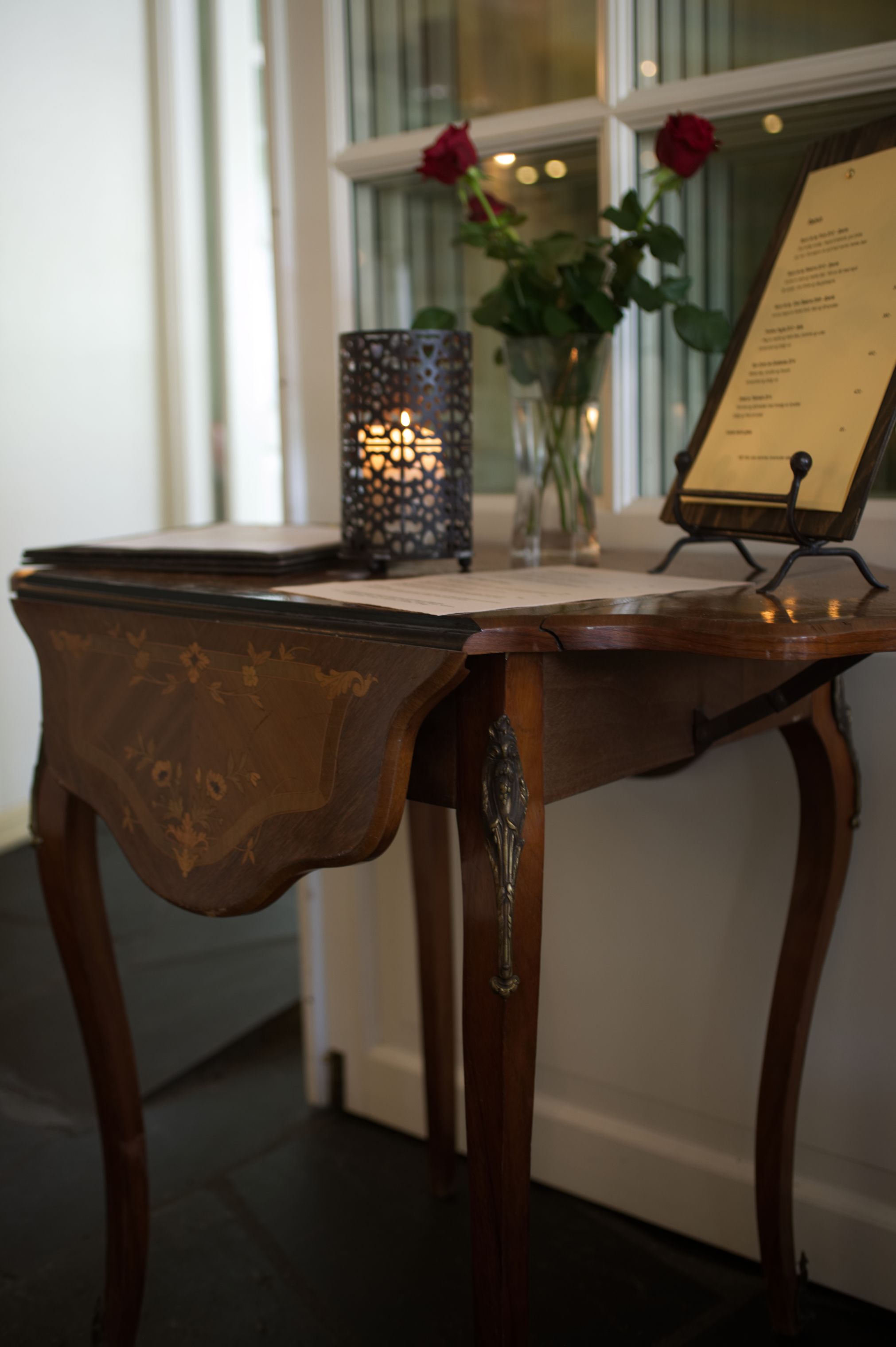 A wooden table with a menu stand, a candle holder, and a vase with flowers.