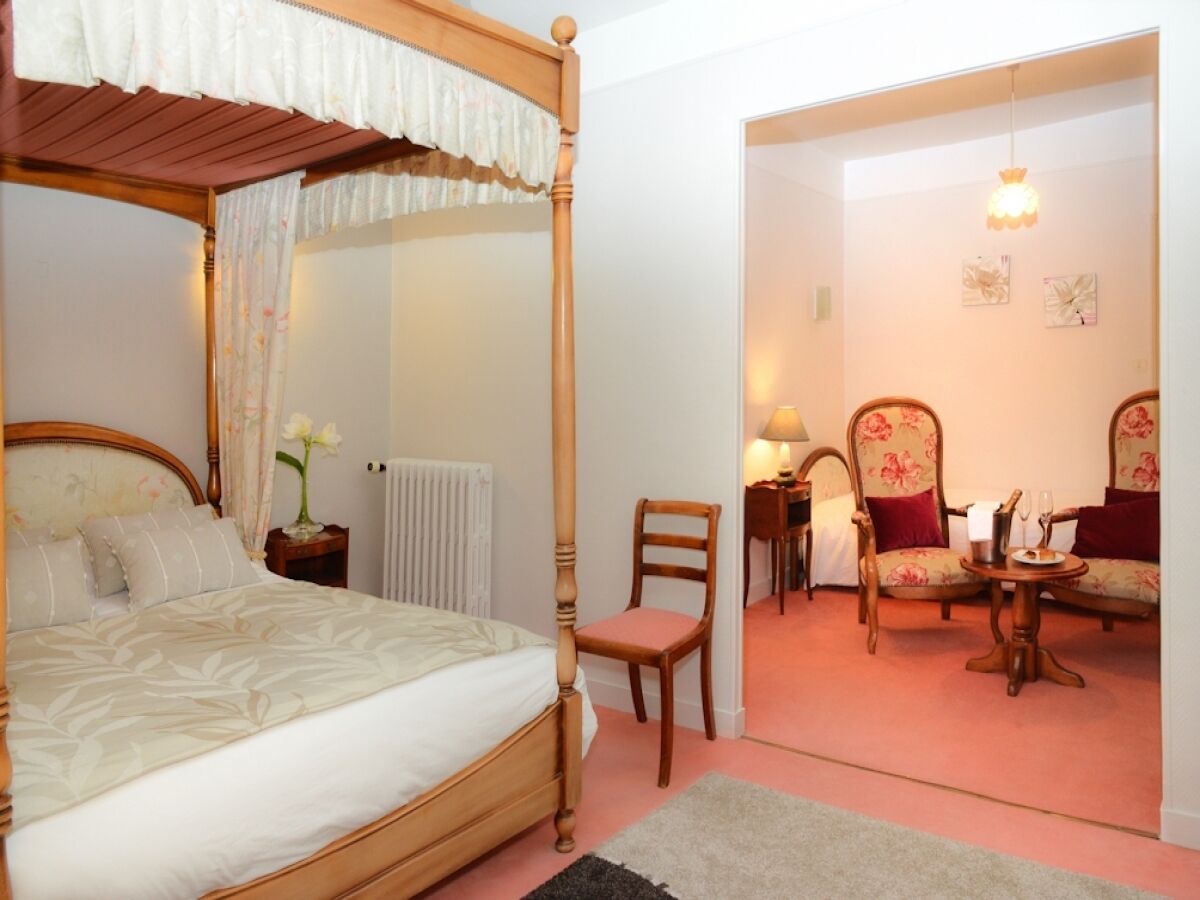 A four-poster bed, a chair, a table with a lamp, and a small table with a plate and a glass.