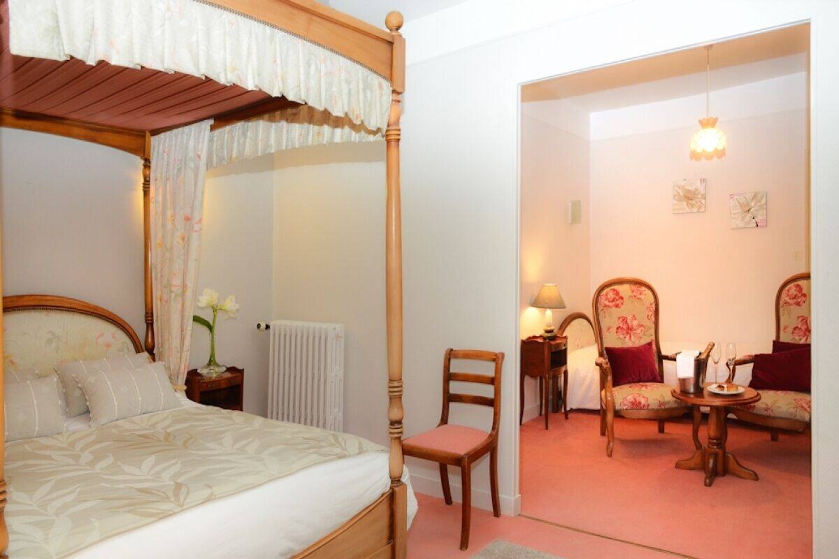 A four-poster bed, a chair, a table with a lamp, and a small table with a plate and a glass.