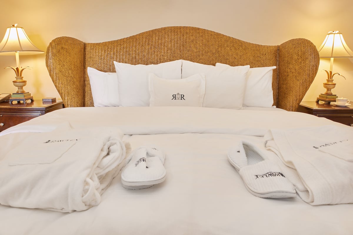 A neatly made bed with white linens and pillows, two bedside tables with lamps, and a pair of slippers on the bed.