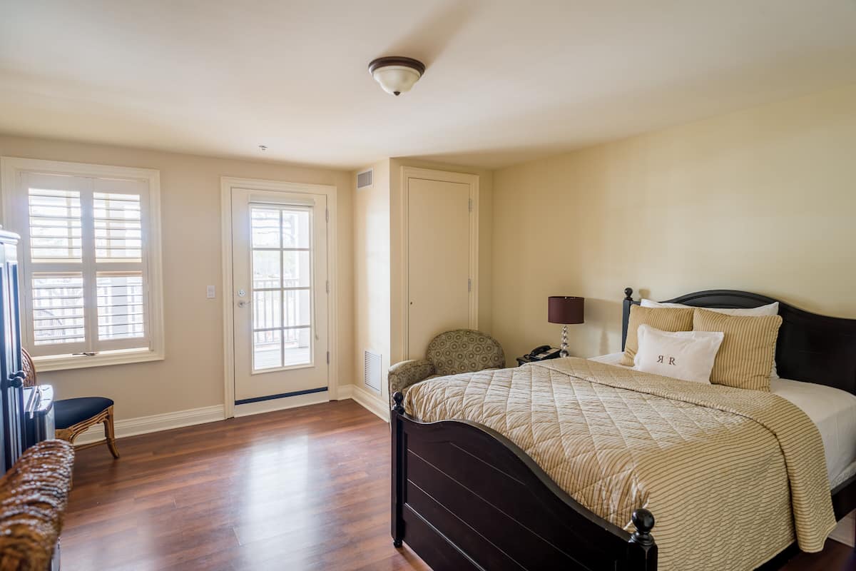 A bedroom with a large bed, a chair, a desk, and a door with windows.