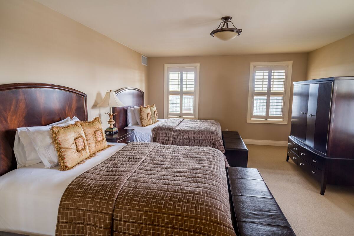 A hotel room with two beds, a bench, a TV, and two windows.