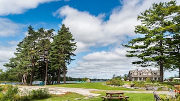 A lakeside property with a large house, picnic tables, and a grassy area with rocks.