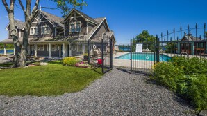 Una casa grande con piscina, un patio cubierto y un jardín cercado.