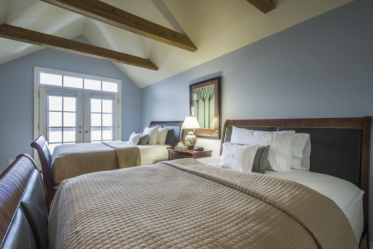 A hotel room with two beds, a large window, and wooden beams on the ceiling.
