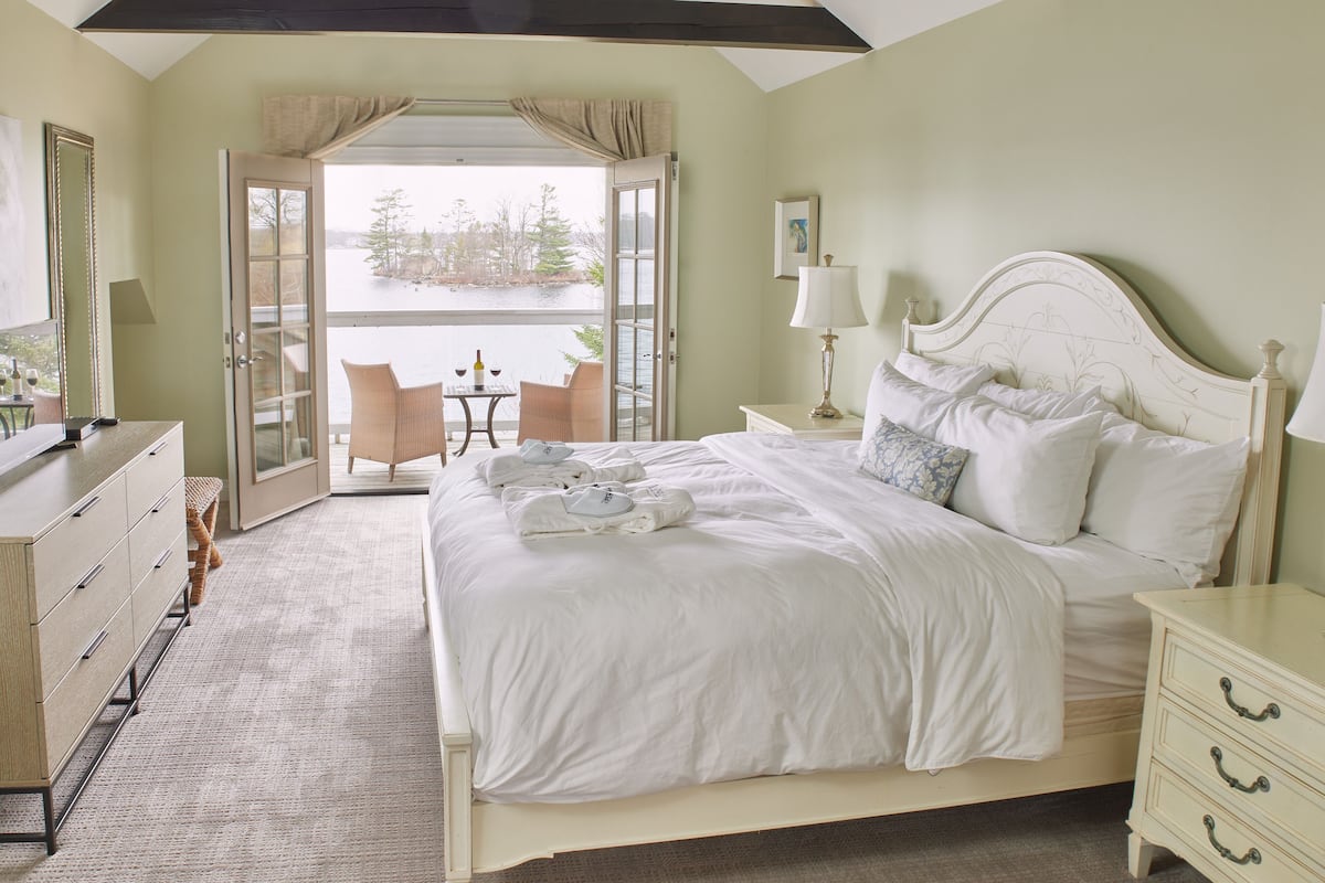 A hotel room with a large bed, a desk with a chair, a dresser, and a view of a body of water through an open door.