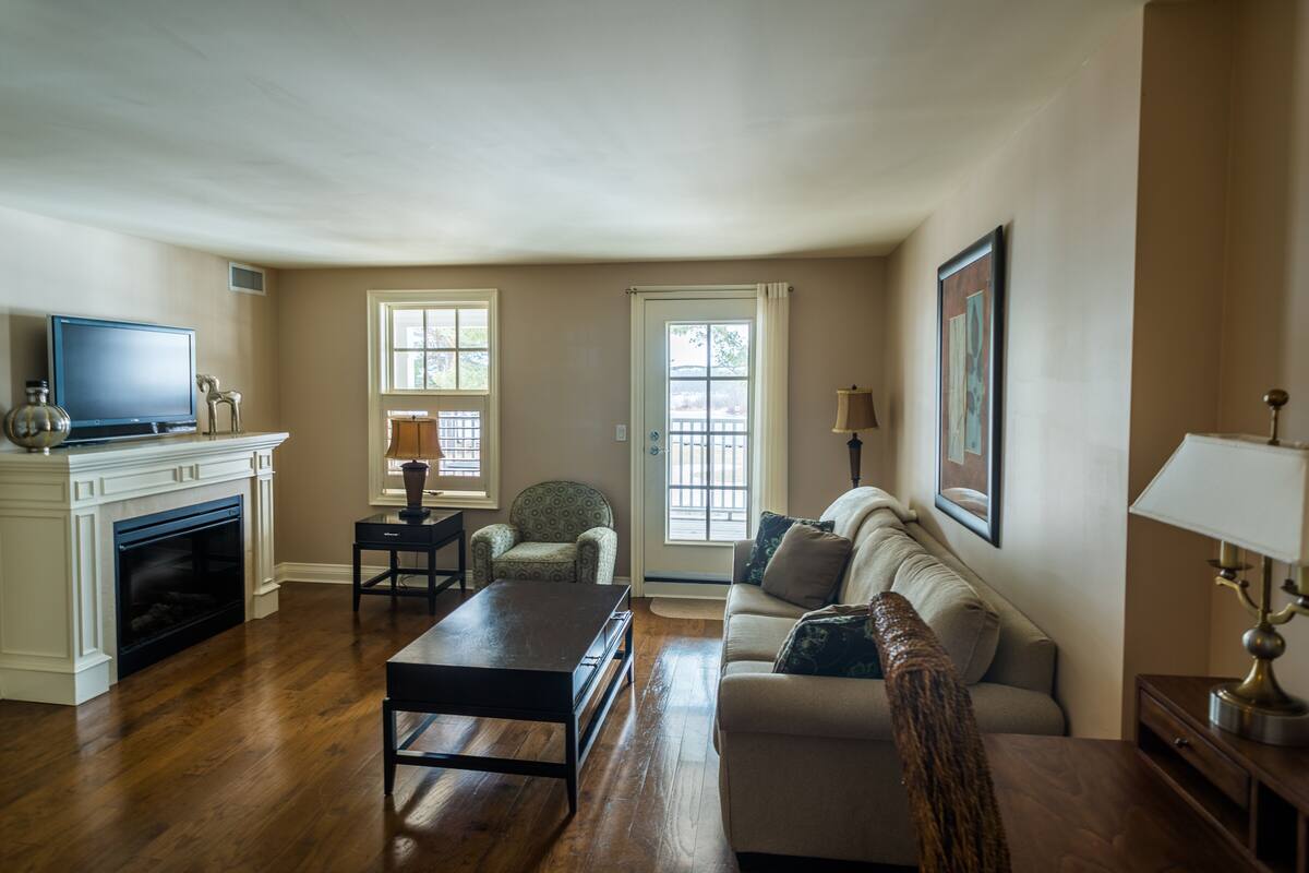 A living room with a fireplace, a sofa, a coffee table, a television, and two windows.
