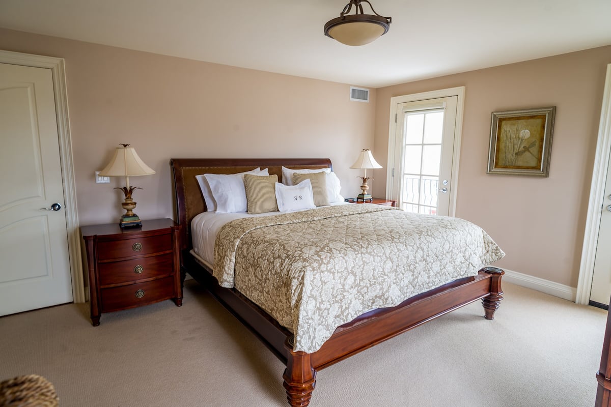 A bedroom with a large bed, two bedside tables with lamps, a door, and a framed picture on the wall.