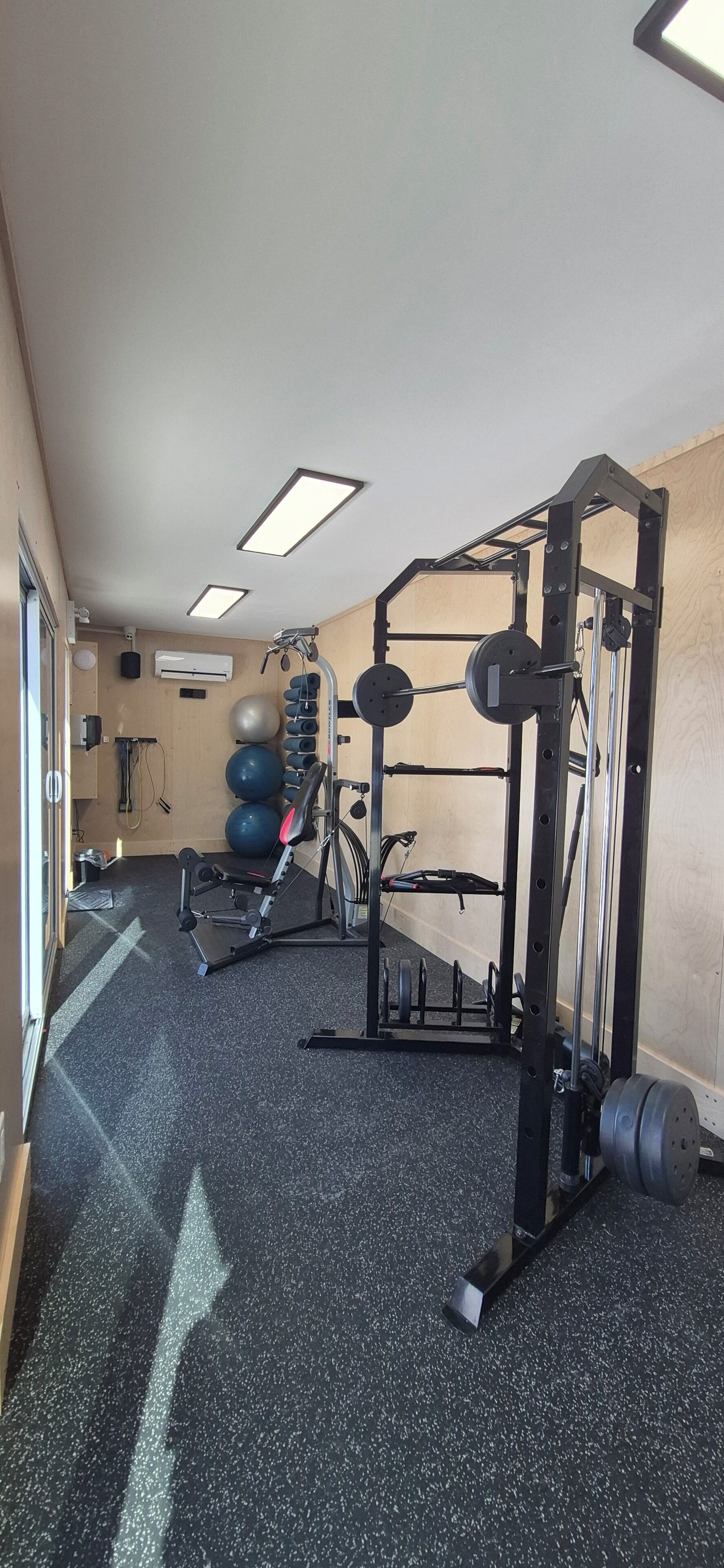 A gym with a weightlifting station, exercise balls, and a treadmill.