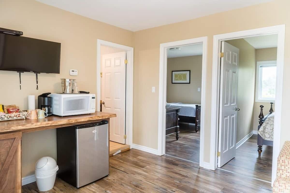A compact kitchen with a microwave, coffee maker, and a small refrigerator. There is a trash bin and a wooden countertop. The room has wooden flooring and beige walls.