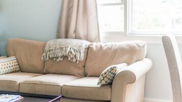 A beige sofa with a throw blanket and patterned pillows, positioned near a window with curtains.