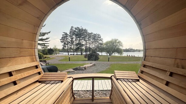 Una terraza de madera con bancos, vistas a un lago y árboles.