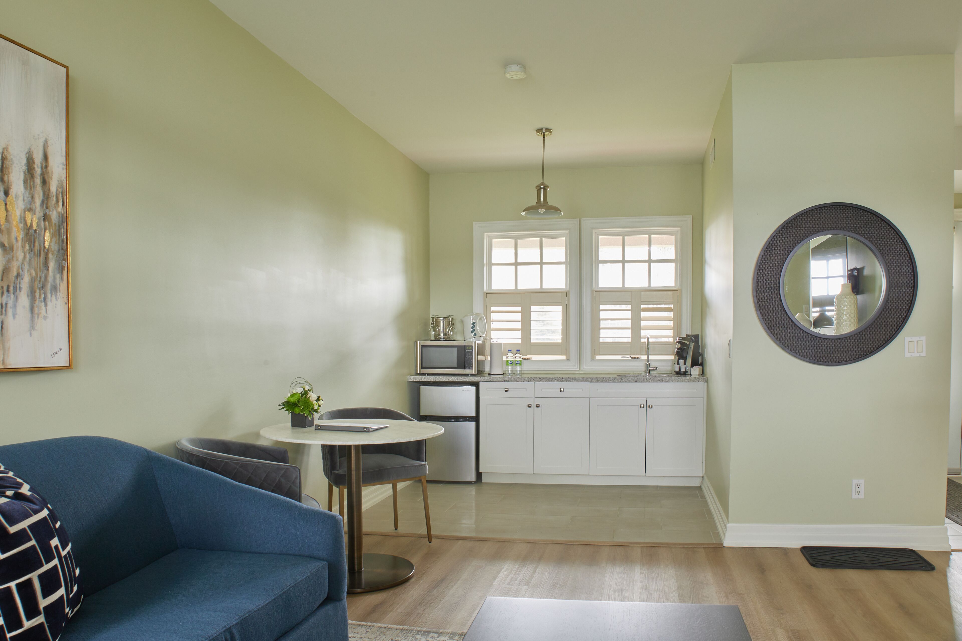 A modern kitchen with white cabinets, a dining area with a blue sofa, and a large mirror on the wall.
