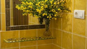 Um banheiro com paredes azulejadas em tons de amarelo, pia branca, prateleira de vidro com artigos de higiene pessoal e espelho com moldura decorativa.