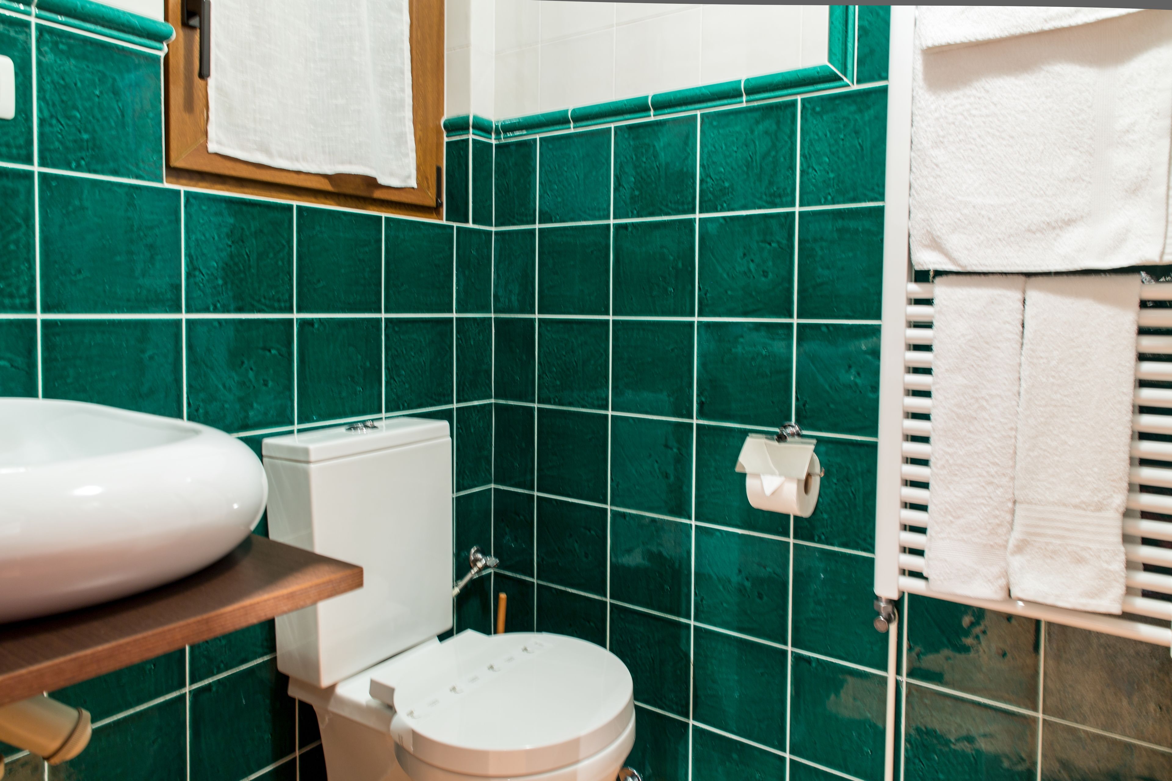 Kylpyhuone, jossa on vihreät laatat, valkoinen pesuallas, wc ja pyyhekoukku.