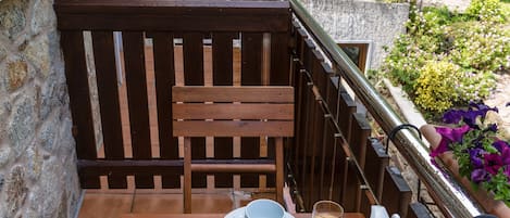 A wooden table set with breakfast items, including eggs, pancakes, and a drink, on a balcony with a stone wall and greenery in the background.