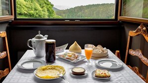 A table set with breakfast items including eggs, toast, and a glass of orange juice, with a scenic view of green hills through a window. - Hotel Rural Fontequeiroso (Muxía)