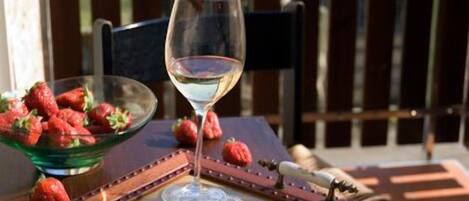 Una mesa con una copa de vino blanco, un cuenco de fresas y un cuadro en un balcón con vistas a las colinas.