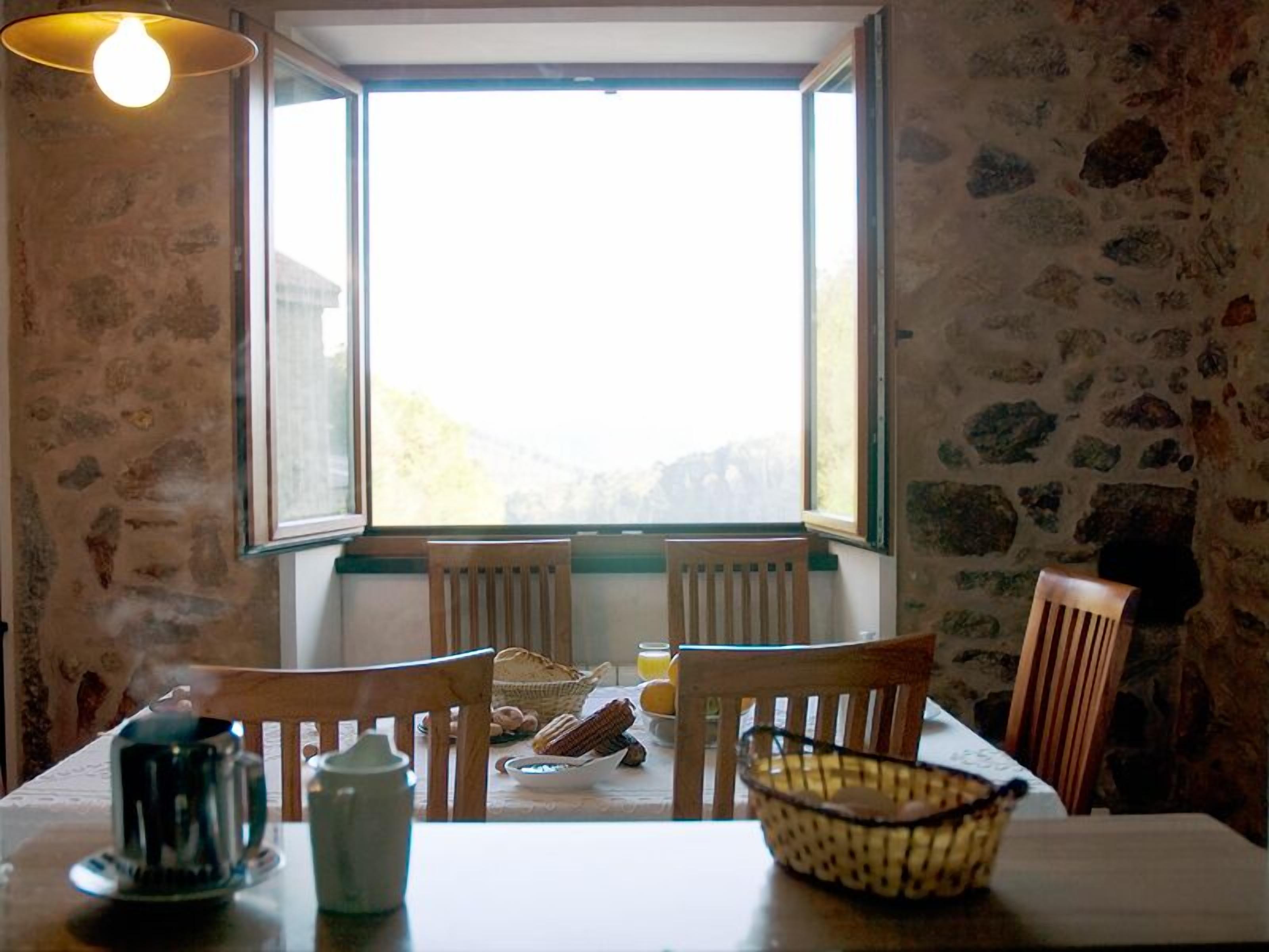 Un comedor con una mesa, sillas, una cafetera, un tazón y una ventana con vistas.