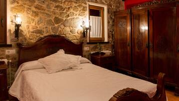 Un dormitorio con pared de piedra, cama de madera con cabecero, armario y ventana con cortina.