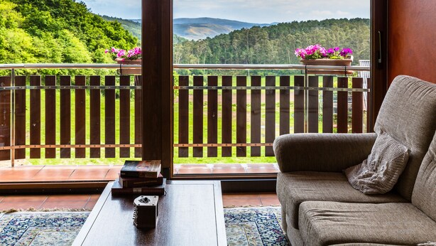 A balcony with a wooden railing, a sofa with a cushion, and a small table with a decorative item. - Hotel Rural Fontequeiroso (Muxía)