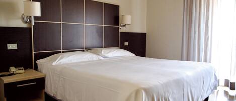 Habitación de hotel con una cama grande, dos mesitas de noche, un teléfono y lámparas de pared.