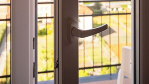 A view from a balcony with a metal railing, a door with a handle, and a clear view of the ocean and buildings in the background. - Hotel Mediterraneo (Lavagna)