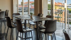 A spacious dining area with a large table and chairs, large windows offering a view of the sea and buildings, and a modern pendant light. - Hotel Mediterraneo (Lavagna)