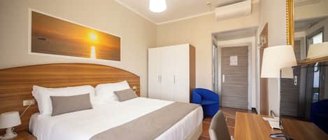 Una habitación de hotel con cama, escritorio, silla, lámpara y espejo.