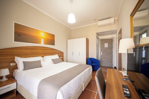 Una habitación de hotel con cama, escritorio, silla, lámpara y espejo.