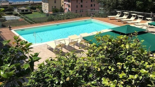 A swimming pool with lounge chairs and umbrellas, surrounded by greenery and a view of the sea. - Hotel Mediterraneo (Lavagna)