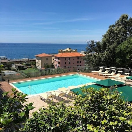 A swimming pool with lounge chairs and umbrellas, surrounded by greenery and a view of the sea.
