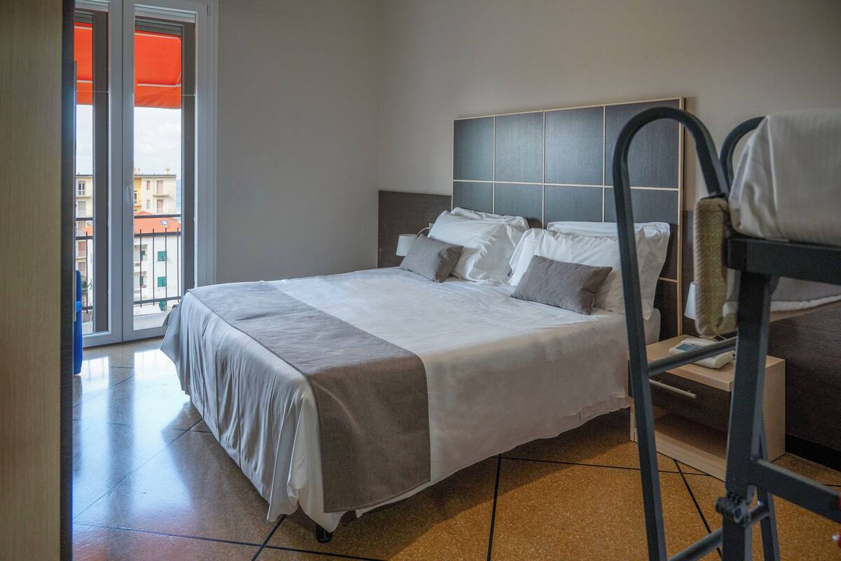 A hotel room with a bed, a bedside table, a chair, and a view of buildings outside.