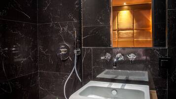 Une salle de bain moderne avec un grand miroir, un lavabo blanc et une douche équipée d’un pommeau de douche à main.