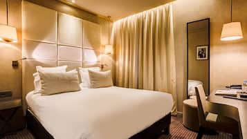 A hotel room with a large bed, a desk, and a chair. There are two lamps on either side of the bed and a mirror on the wall.