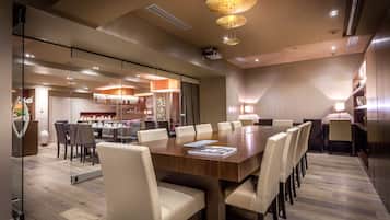 Un salón de conferencias con una amplia mesa de madera, sillas blancas y luminarias modernas.