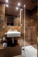 Une salle de bain moderne avec une douche à parois de verre, un mur recouvert de carreaux de marbre et un lavabo blanc agrémenté d’articles de toilette.