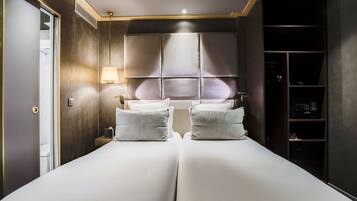 Una habitación de hotel con una cama grande, dos mesitas de noche, un armario y una ventana con persianas.