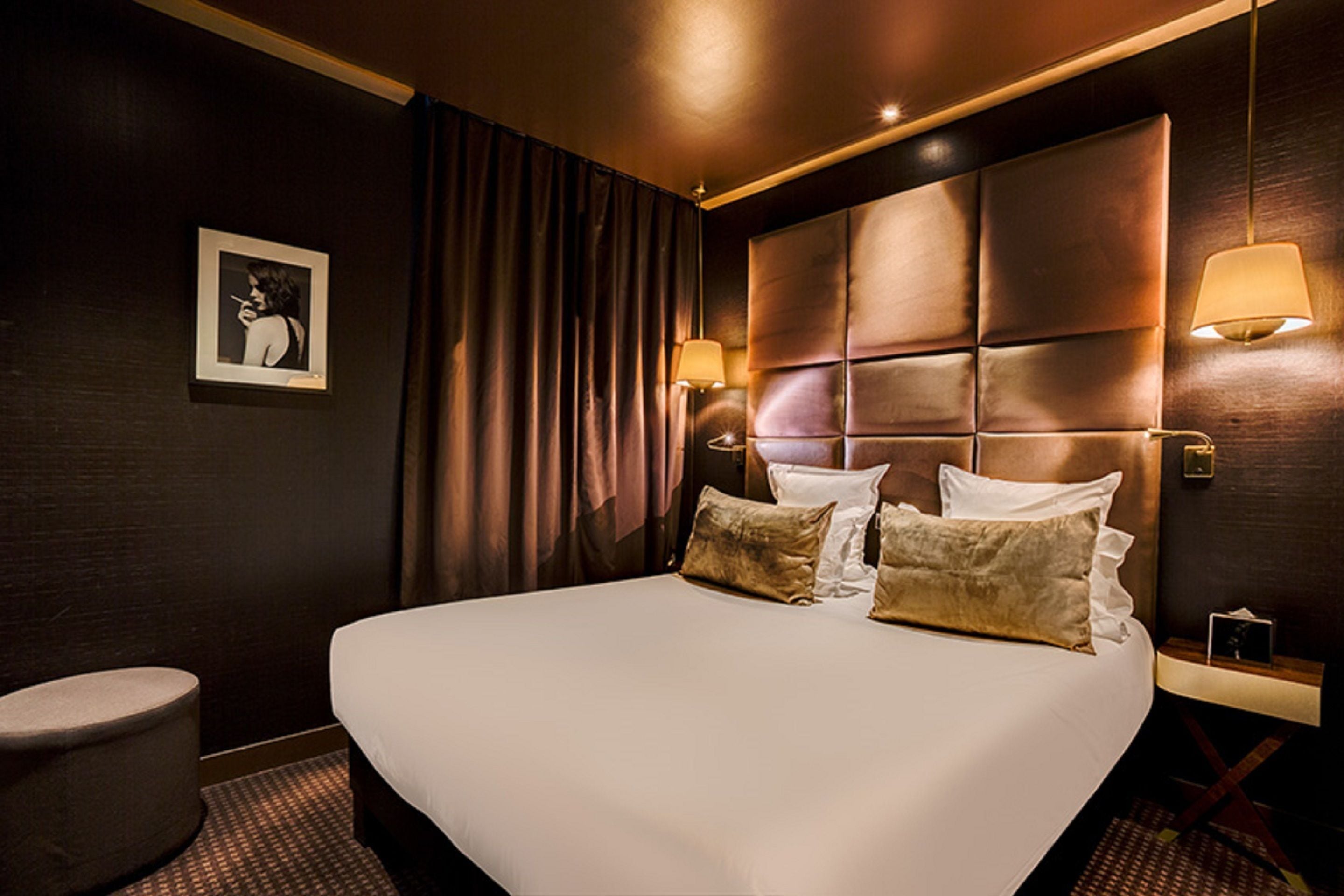 A hotel room with a large bed, a headboard with panels, a bedside table with a lamp, and a framed picture on the wall.
