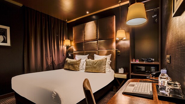 Une chambre d’hôtel avec un grand lit, des tables de chevet, un bureau avec un ordinateur portable et une lampe.