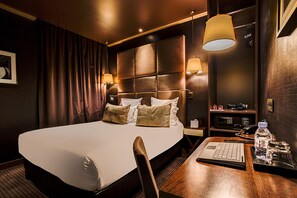 Una habitació d'hotel amb un llit gran, taules de nit, un escriptori amb un ordinador portàtil i una làmpada.