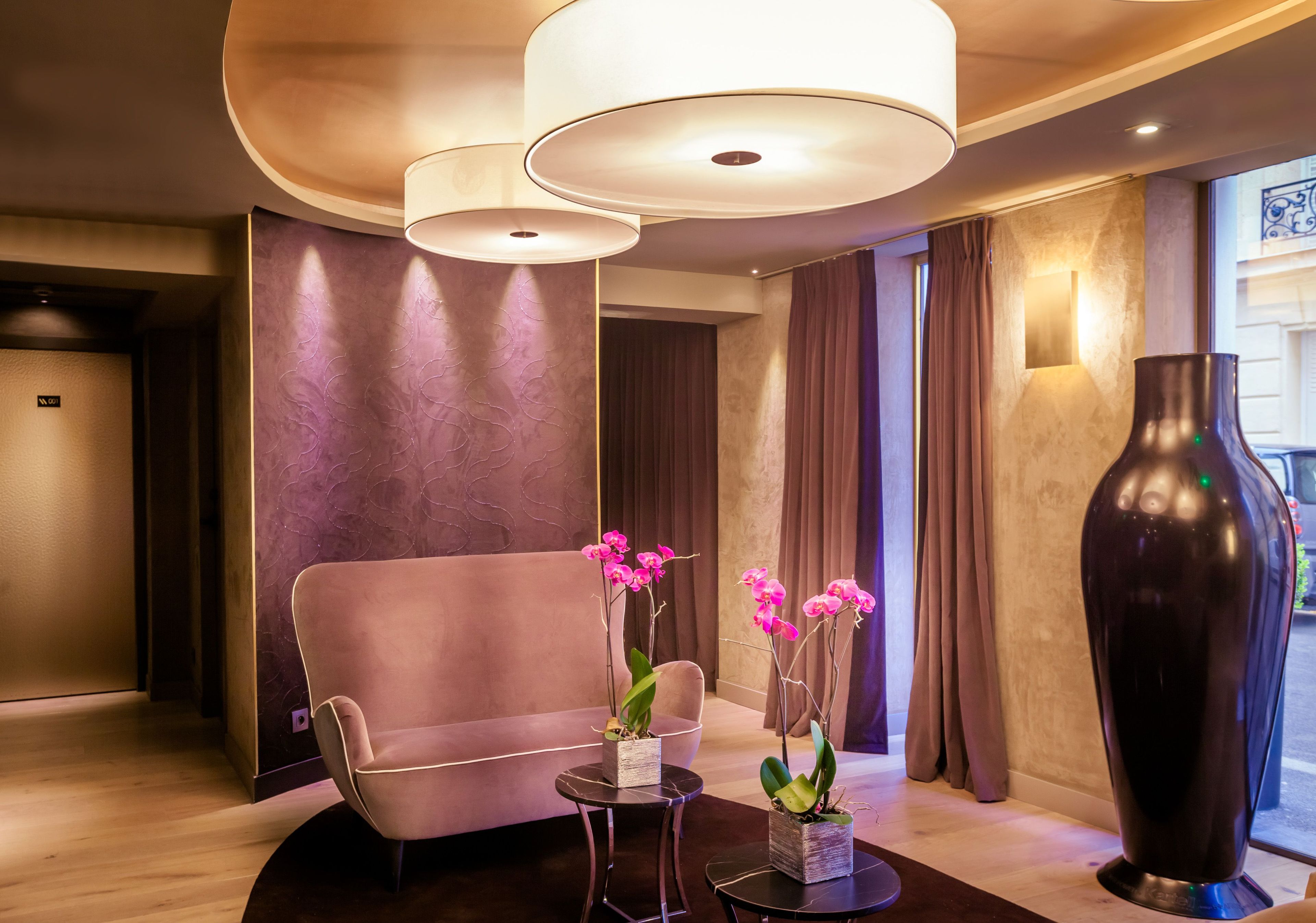 A modern lobby with a sofa, two small tables with potted orchids, a large vase, and pendant lighting.
