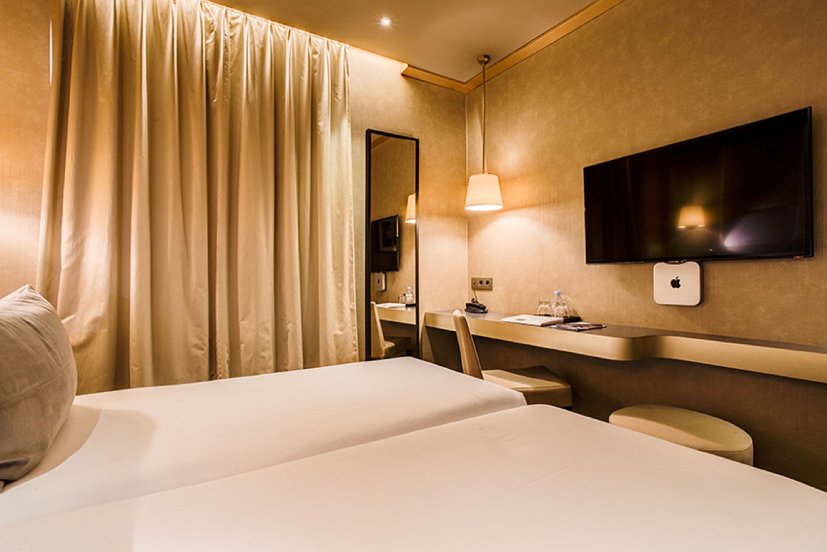 A hotel room with two beds, a desk, a chair, a TV, and a mirror.