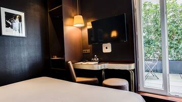 Habitación de hotel con cama, escritorio con silla, televisor montado en la pared y ventana con vista a zonas verdes.