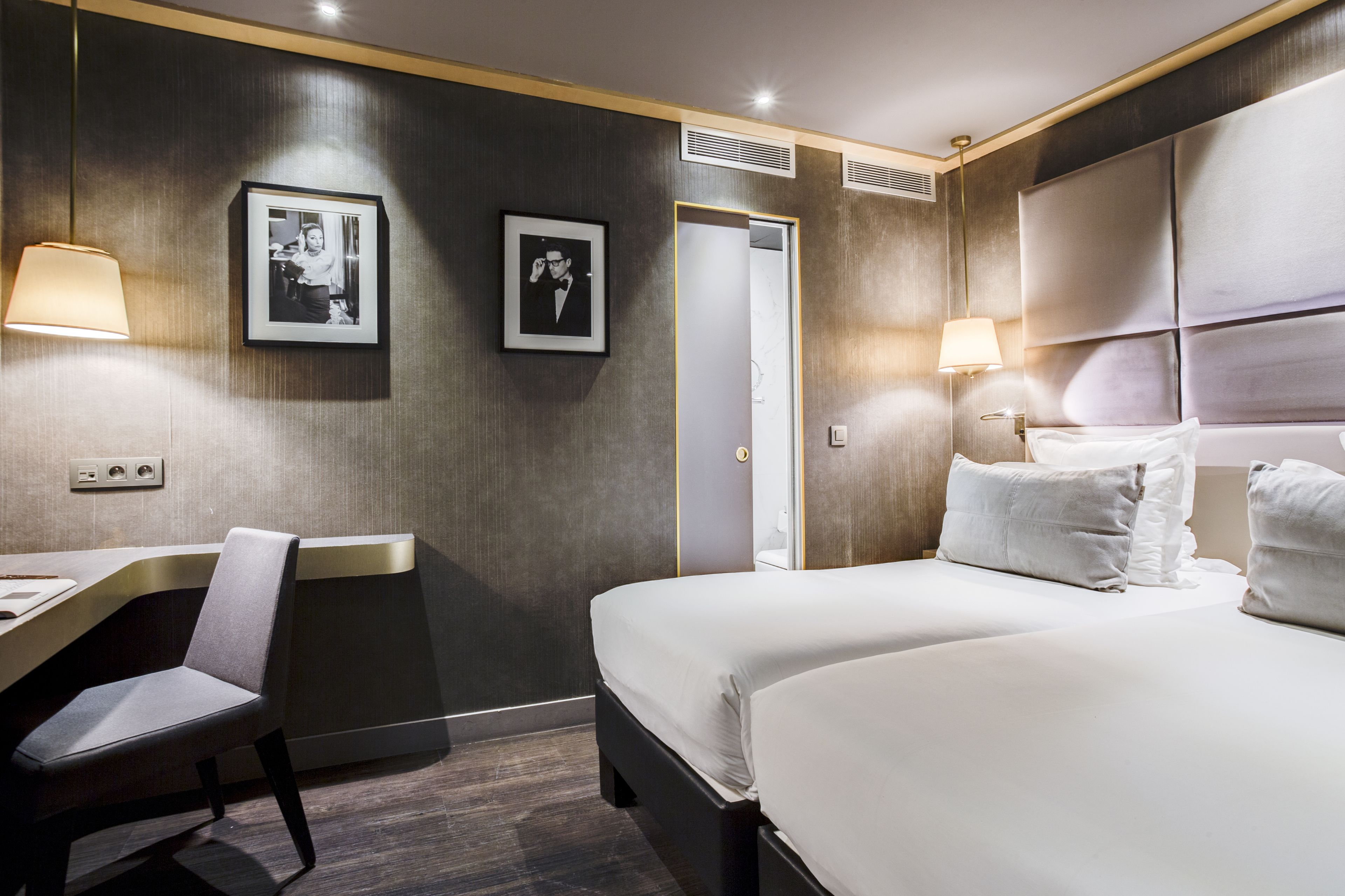 Una habitación de hotel con una cama, un escritorio, una silla, dos cuadros en la pared y una puerta.