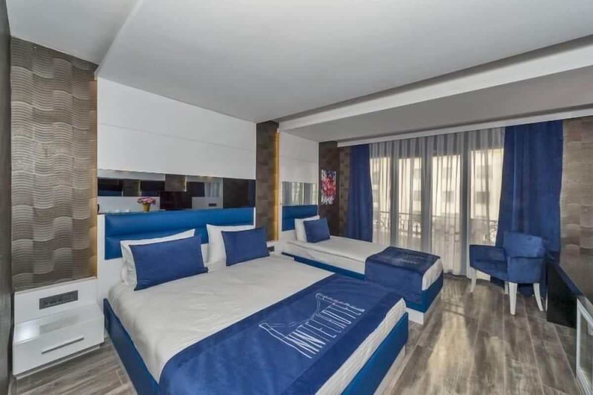 Une chambre d’hôtel moderne avec deux lits, un coin salon et une grande fenêtre avec des rideaux.